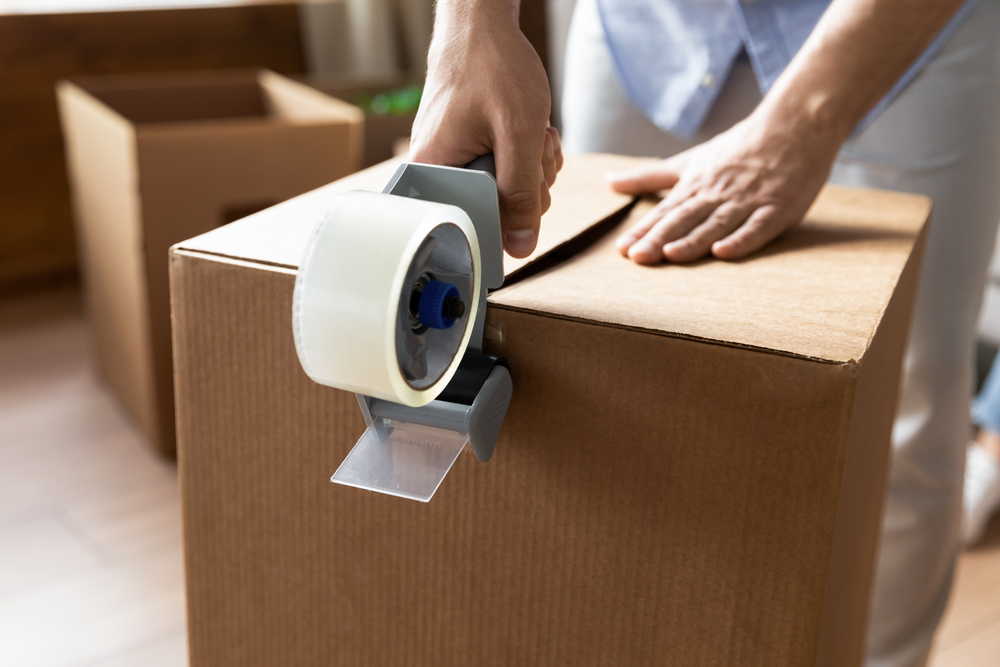 Professional mover packing a moving box shut.