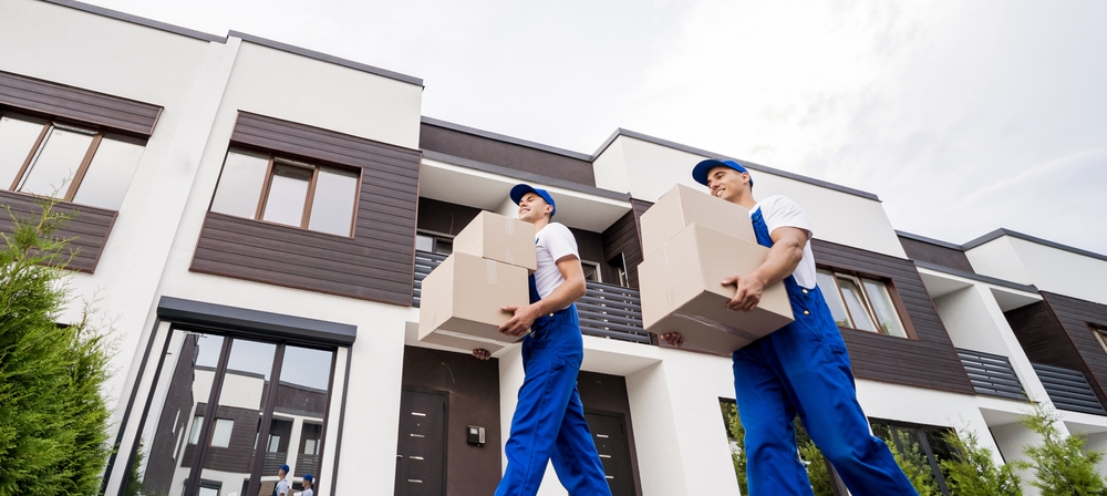 two professional movers carrying moving boxes outside.